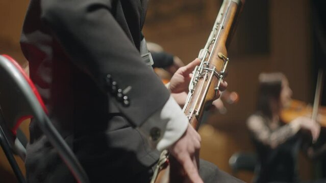 bassoon in small orchestra, male musician is playing music, wind instrument in hand of bassoonist