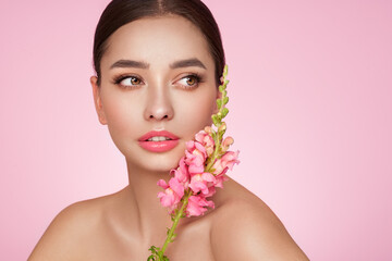 Naklejka na ściany i meble Portrait beautiful young woman with clean fresh skin. Model with healthy skin, close up portrait. Cosmetology, beauty and spa. Girl with a pink flower