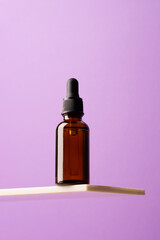 Bottle of cosmetic product, dark glass with pipette creative marble shelf, podium purple background