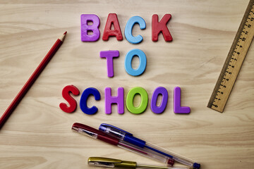 the phrase back to school is laid out in multicolored letters on the table next to colored pencils fountain pens and a ruler the concept of education school