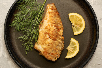 fried fish with lemon and herbs in a frying pan on the table