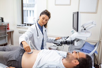 Young male patient lying on bed and having ultrasound examination of abdomen in medical clinic