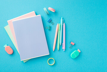 Back to school concept. Top view photo of colorful stationery stack of notebooks pineapple shaped erasers adhesive tape binder clips and pens on isolated blue background