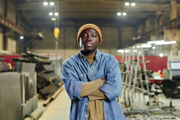 Fototapeta na wymiar Portrait of African young worker in casual clothing standing at factory with his arms crossed and looking at camera