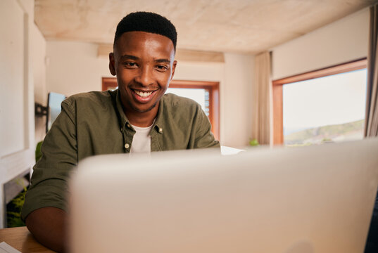 Close up portrait of a happy Young adult black African-American male smiling while using his laptop. Remote working from his modern apartment