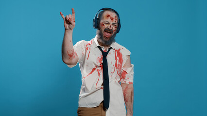 Messy creepy zombie wearing electronic wireless headphones while listening to music on blue...