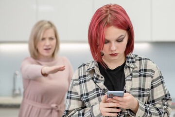 Angry woman scolds her teenage daughter, girl uses smartphone and ignores her mom. Family...