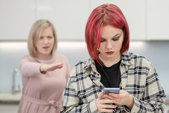 Angry woman scolds her teenage daughter, girl uses smartphone and ignores her mom. Family relationships