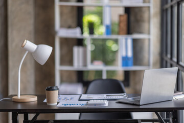 Laptop Computer, notebook, and eyeglasses sitting on a desk in a large open plan office space after...