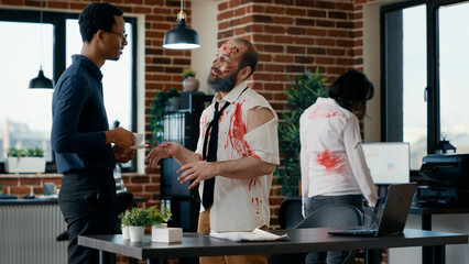 African american businessman discussing with infected brain-eating zombie colleague in office workspace. Dead walking corpse with deep and bloody wounds talking with doomsday survivor.