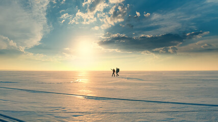 The couple of travelers walking through the snow field on sunset background