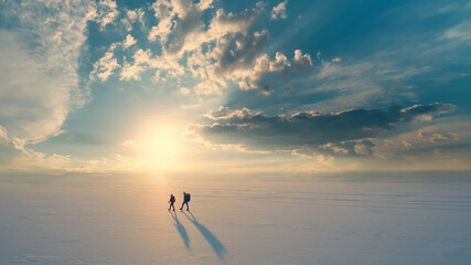 The two people with backpacks going through the snow field against beautiful sky