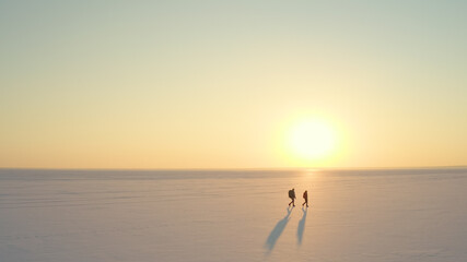 Fototapeta na wymiar The two people with backpacks going through the snow field against beautiful sky