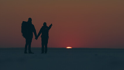 The two tourists going through the snow field against beautiful sunset