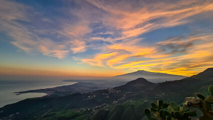 Naklejka premium Panoramic view on silhouette of hills during twilight. Watching beautiful sunset behind volcano Mount Etna near Castelmola, Taormina, Sicily, Italy, Europe, EU. Clouds with vibrant red orange colors