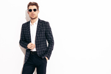 Portrait of handsome confident stylish hipster lambersexual model. Sexy modern man dressed in black elegant suit. Fashion male posing in studio near white wall. In sunglasses
