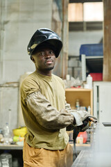 Portrait of African industrial welder looking at camera while working with welding torch at factory