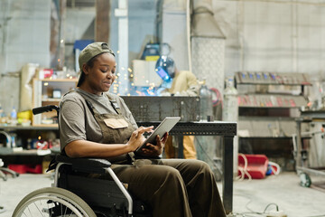 African female worker with disability using digital tablet at work while sitting in wheelchair at...