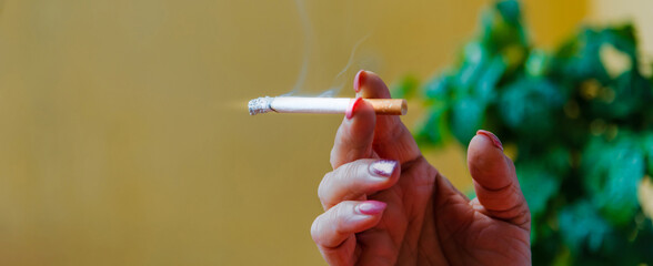 Middle age woman smoking cigarette.Close up of a female hand holding cigarette.copy space.Blurred background.Side view.Banner,advertisement.