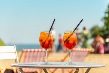 Two glasses of orange spritz aperol drink cocktail on table outdoors with sea and trees view...