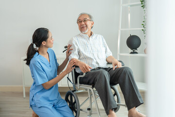 Young Asian woman caregiver doctor during home visit talking encourage to senior elderly patient while sitting on wheelchair
