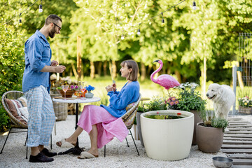 Young stylish couple hang out together with a drink at their beautiful backyard of country house on nature. Man and woman spend summertime outdoors