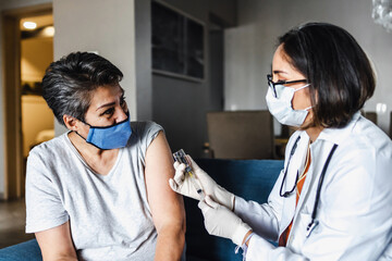 Hispanic female Doctor giving Covid vaccine to senior woman in her home in Mexico Latin America