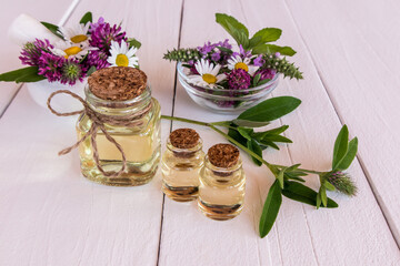 natural cosmetic in glass bottles on a white wooden table. chamomile flowers, clover, mint in bowls. natural organic care.