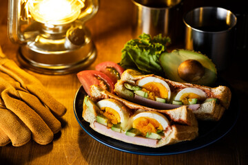 木製のテーブルにホットサンドとコーヒーとランタンの夜のキャンプ飯