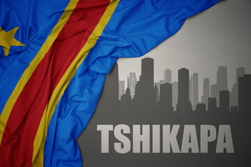 abstract silhouette of the city with text Tshikapa near waving colorful national flag of democratic...