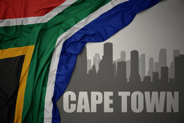 abstract silhouette of the city with text Cape Town near waving colorful national flag of south...