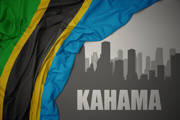 abstract silhouette of the city with text Kahama near waving colorful national flag of tanzania on a gray background.
