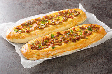 Pastrmajlija is an oval shaped pizza dough dressed with meat in the center and topped with an egg wash closeup on the parchment on the table. Horizontal