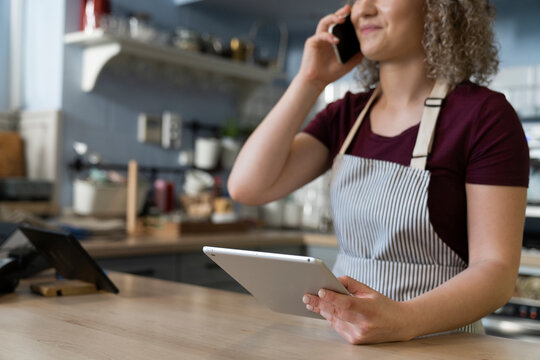Young caucasian waitress using digital tablet and phone at work in the cafe