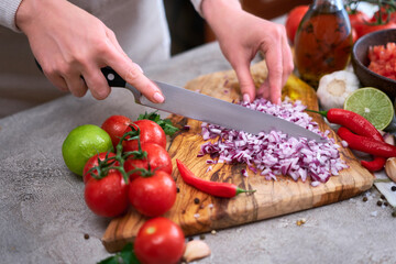 woman cutting and chopping onion by knife on wooden board