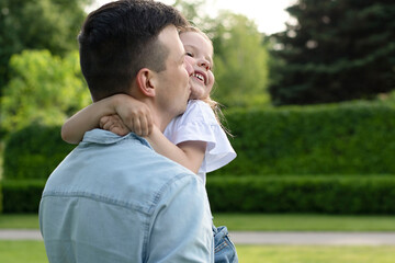 A family. Dad holds his daughter in his arms and hugs tightly in the park in the summer.