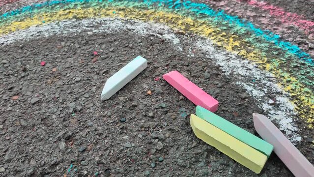 Colored crayons on the pavement and a painted rainbow. The rainbow is drawn with colored crayons on the road.