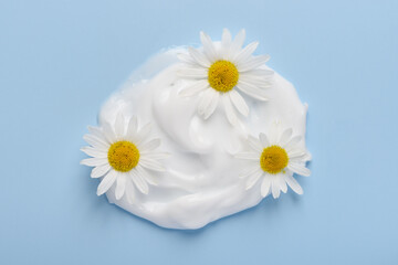 Obraz premium White cosmetic cream with chamomile flowers on blue background top view