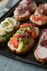Open sandwiches with salmon, avocado, radish, tomatoes, microgreens and eggs close-up on a black tray. A variety of healthy food. Beautiful table setting