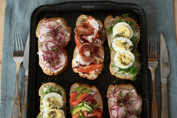 Open sandwiches with salmon, avocado, radishes, tomatoes, feta cheese, bacon, microgreens and eggs on a black tray. flat lay. A variety of healthy food. Beautiful table setting