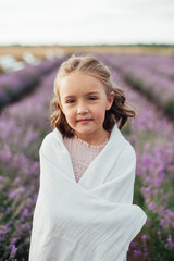 close view of a pretty smiling girl with a cute hairstyle wearing pink dress covered with a ivory blanket on the background of lavender field