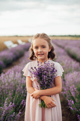 vertical photo of a cute little girl in pink dress with a bouquet in hands standing among lavender bushes