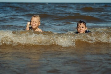 7-8 years old cute caucasian boys swimming in the sea with big splashes in waves