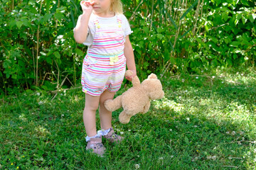 little child 3 years old, girl in striped shorts in green meadow, teddy bear in hand, concept of...