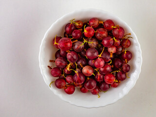 Fresh, sweet red gooseberries in a white cup on a white background.