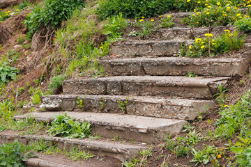 An old dilapidated concrete staircase on an earthen slope is overgrown with grass. Iron...