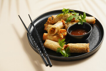 Traditional southeast asian starter dish spring or summer rolls - deep fried dim sum dumplings stuffed with vegetables with sweet-sour sauce and fresh coriander on black plate with black chop sticks