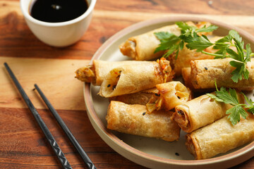 Traditional southeast asian starter dish spring or summer rolls - deep fried dim sum dumplings stuffed with vegetables with soy sauce, fresh coriander on grey plate with black chop sticks, wooden