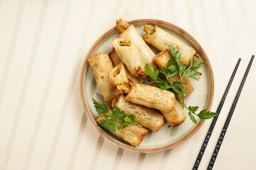 Traditional southeast asian starter dish spring or summer rolls - deep fried dim sum dumplings stuffed with vegetables with soy sauce, fresh coriander on grey plate with black chop sticks, top view