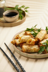 Traditional southeast asian starter dish spring or summer rolls - deep fried dim sum dumplings stuffed with vegetables with soy sauce, fresh coriander on grey plate with black chop sticks, top view